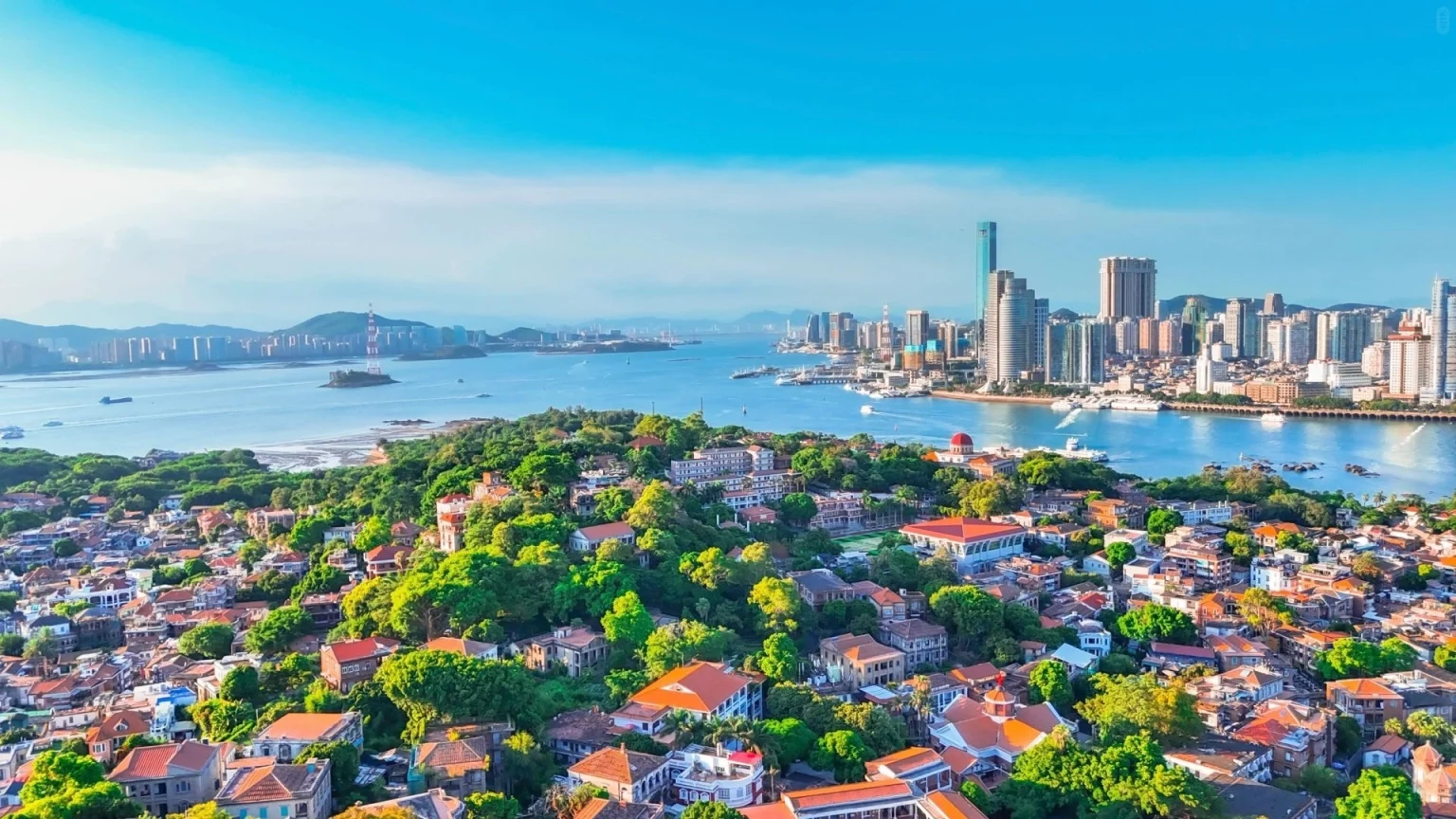 Vista aérea de la isla de Gulangyu y el paisaje urbano de Xiamen con la costa exuberante y los vibrantes tejados bajo un cielo azul brillante - Fujian, hogar de las creencias Mazu, Nanyin y Hakka Tulou 2026 - El viaje a China - Provincias de China - Descubre la cultura y el patrimonio regional - El viaje a China Vista aérea de la isla de Gulangyu y el paisaje urbano de Xiamen con la costa exuberante y los vibrantes tejados bajo un cielo azul brillante - Fujian, hogar de las creencias Mazu, Nanyin y Hakka Tulou 2026 - El viaje a China - Provincias de China - Descubre la cultura y el patrimonio regional - El viaje a China