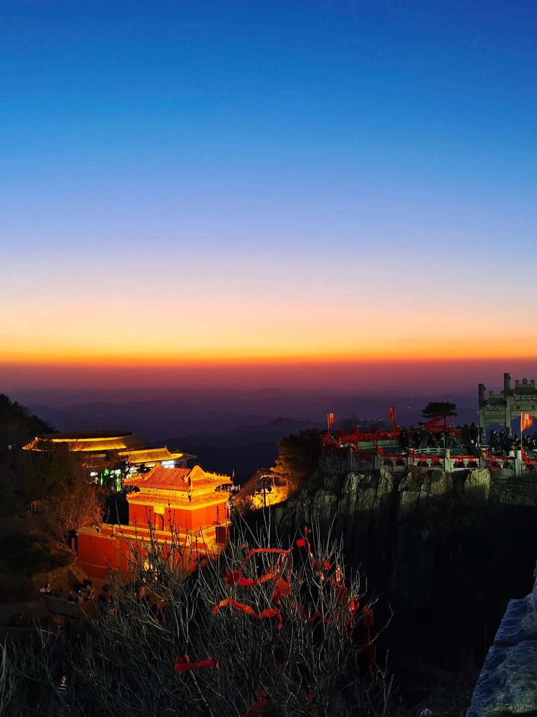 Taishan at dusk traditional buildings illuminated surrounded by the silhouette of mountains under a clear gradient sky