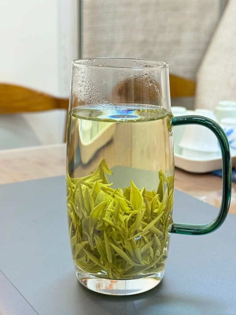A clear glass mug with Huangshan Maofeng tea leaves steeping releasing their fresh aroma and light green color