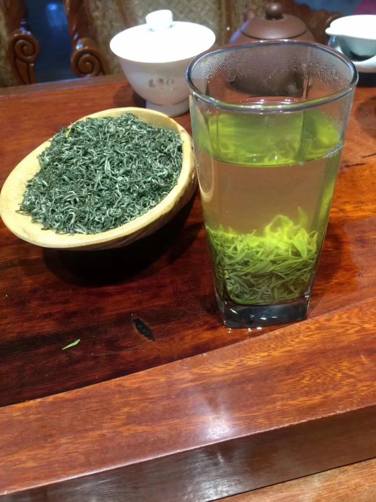 A glass of steeped Duyun Maojian tea with dried leaves on display illustrating its clarity and freshness