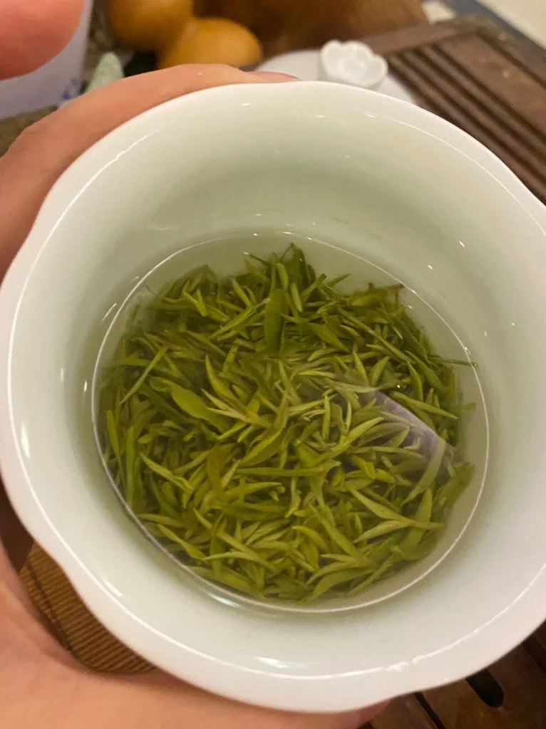 A porcelain cup of freshly steeped Xinyang Maojian tea leaves emphasizing the clarity of the brew and leaf quality