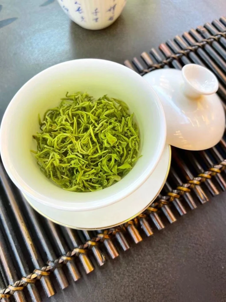 A porcelain gaiwan with steeped Biluochun tea leaves on a bamboo mat