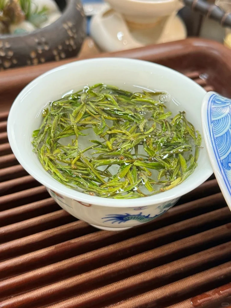 A traditional Chinese tea bowl filled with steeping Huangshan Maofeng tea leaves releasing a delicate aroma