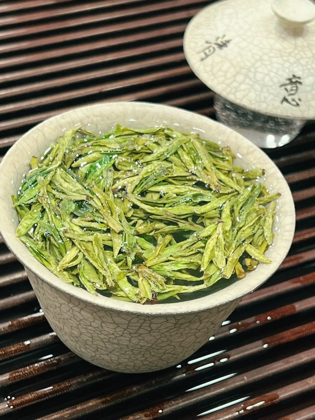 Brewed West Lake Longjing tea in a ceramic cup with vibrant green leaves