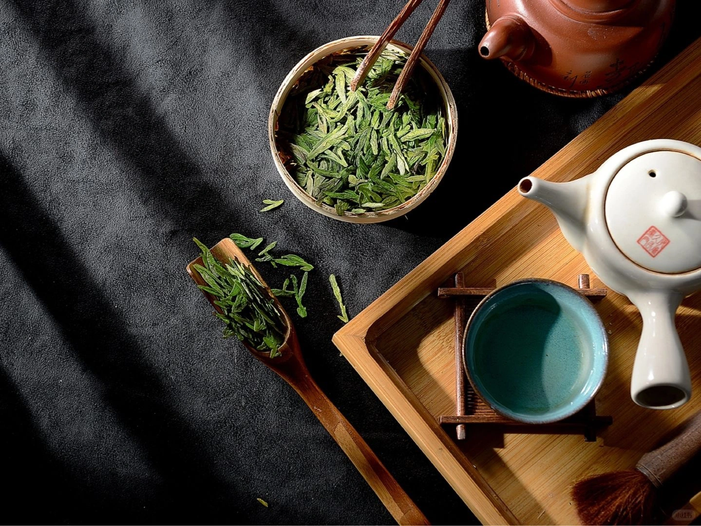 Chinesische Teezubereitungsanlage mit Longjing-Teeblättern, traditioneller Teekanne und Teezubehör auf einem Holztablett