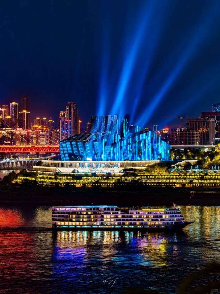 Chongqing Grand Theatre at night with stunning blue light beams and a riverboat below