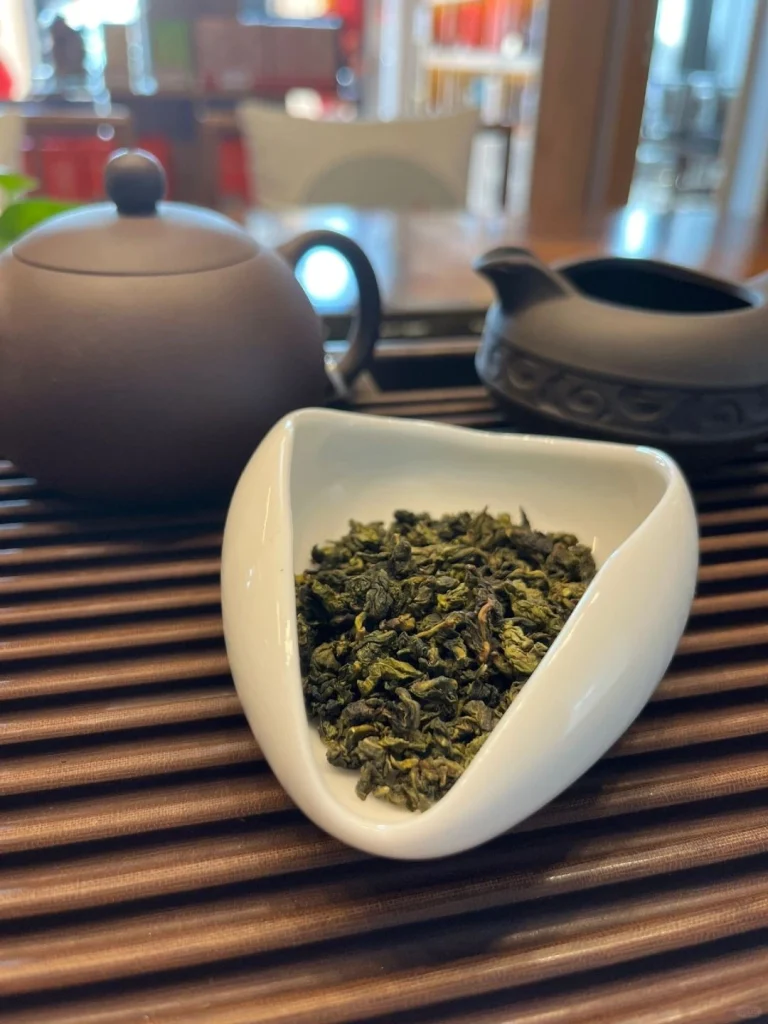 Dried Tieguanyin Tea Leaves in a White Ceramic Dish with Teapot Background