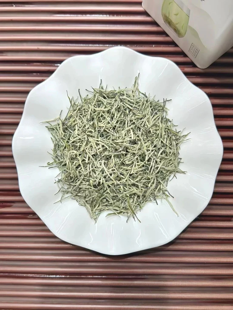 Dried Xinyang Maojian tea leaves arranged neatly on a white plate highlighting their thin and wiry shape