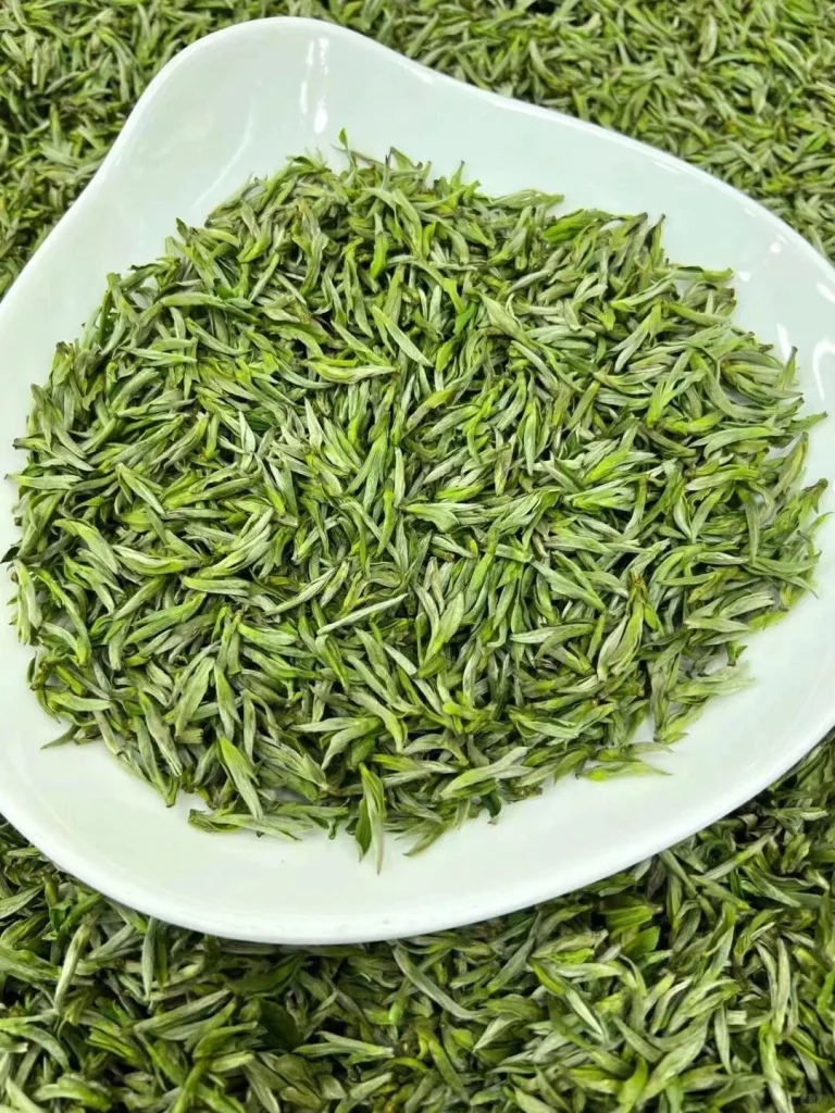 Freshly dried Huangshan Maofeng tea leaves on a white plate showcasing their delicate green tips and vibrant color