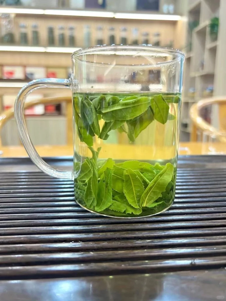 Glass mug showcasing Luan Guapian green tea steeping with vibrant fresh leaves