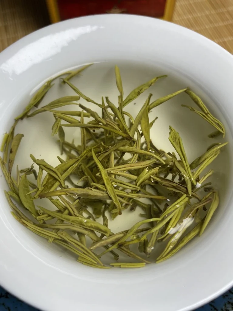 Infusion of Junshan Yinzhen tea leaves in a white ceramic bowl capturing its golden liquor