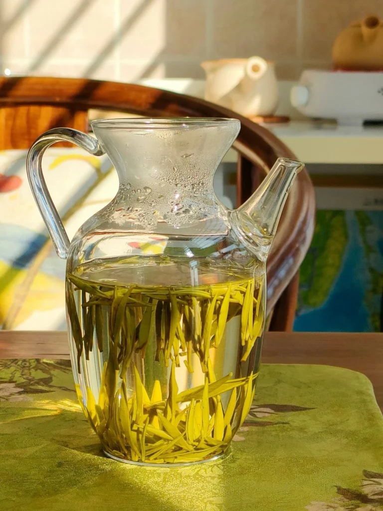 Junshan Yinzhen tea steeping in a clear glass teapot with golden hues