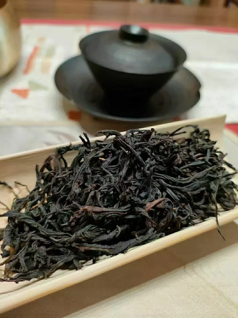Loose leaf Keemun black tea on a bamboo tray with a black gaiwan in the background