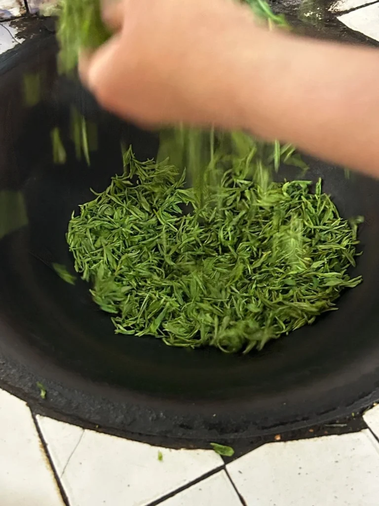 Stir frying fresh Huangshan Maofeng leaves in a wok to enhance their flavor and aroma during processing
