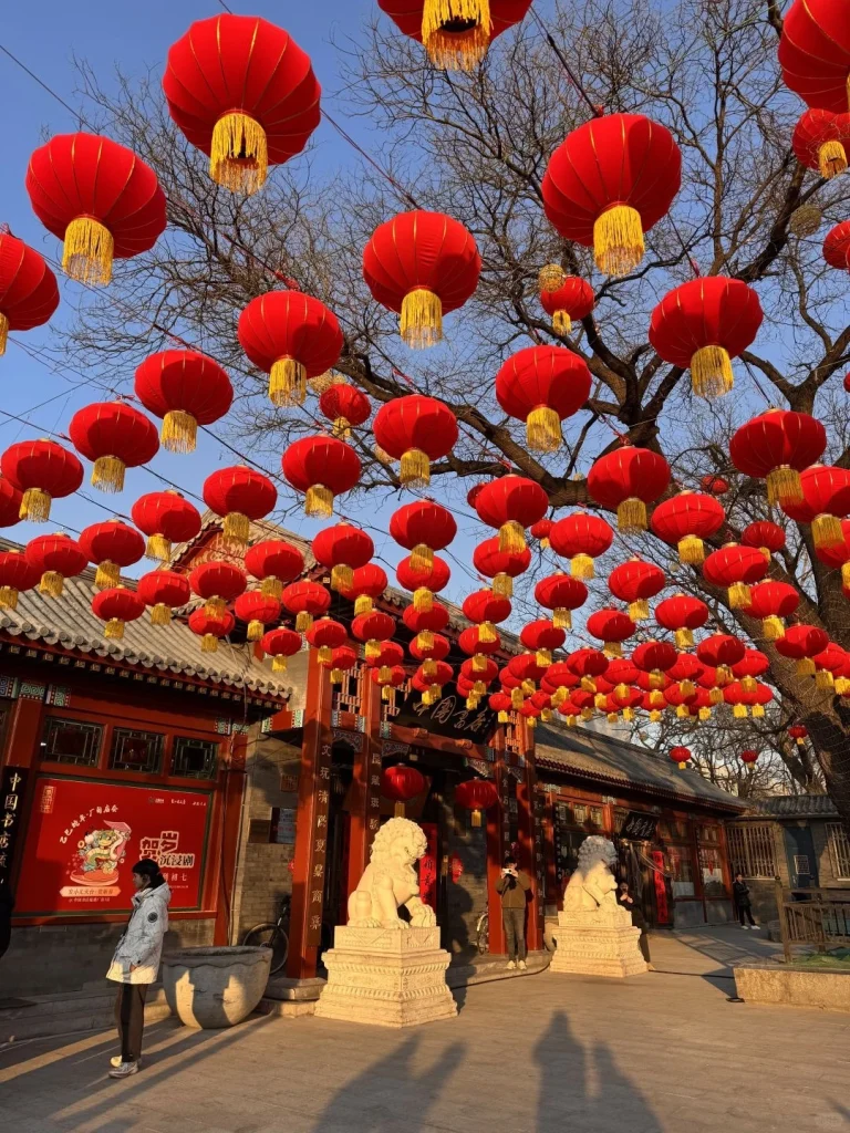A traditional Beijing courtyard adorned with red lanterns and lion statues under clear blue skies