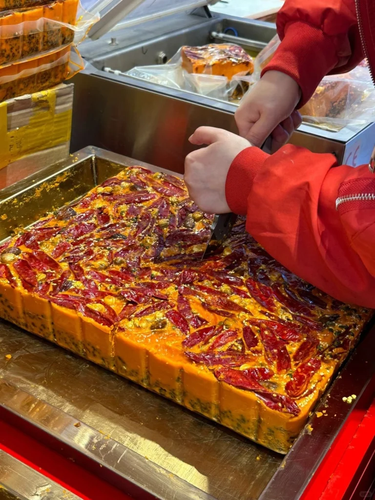A chef cutting spicy hotpot base at the restaurant with chili peppers and seasoning visible