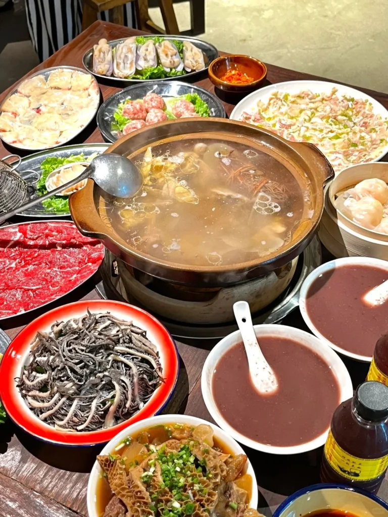 A close up of a bubbling hotpot filled with a rich broth accompanied by fresh ingredients in a traditional style