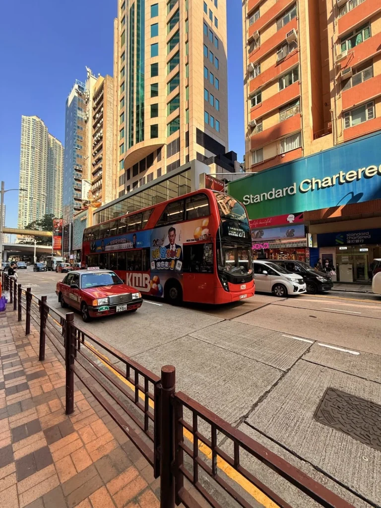 A double decker bus traveling through a busy street in Hong Kong with high rise buildings and advertisements around