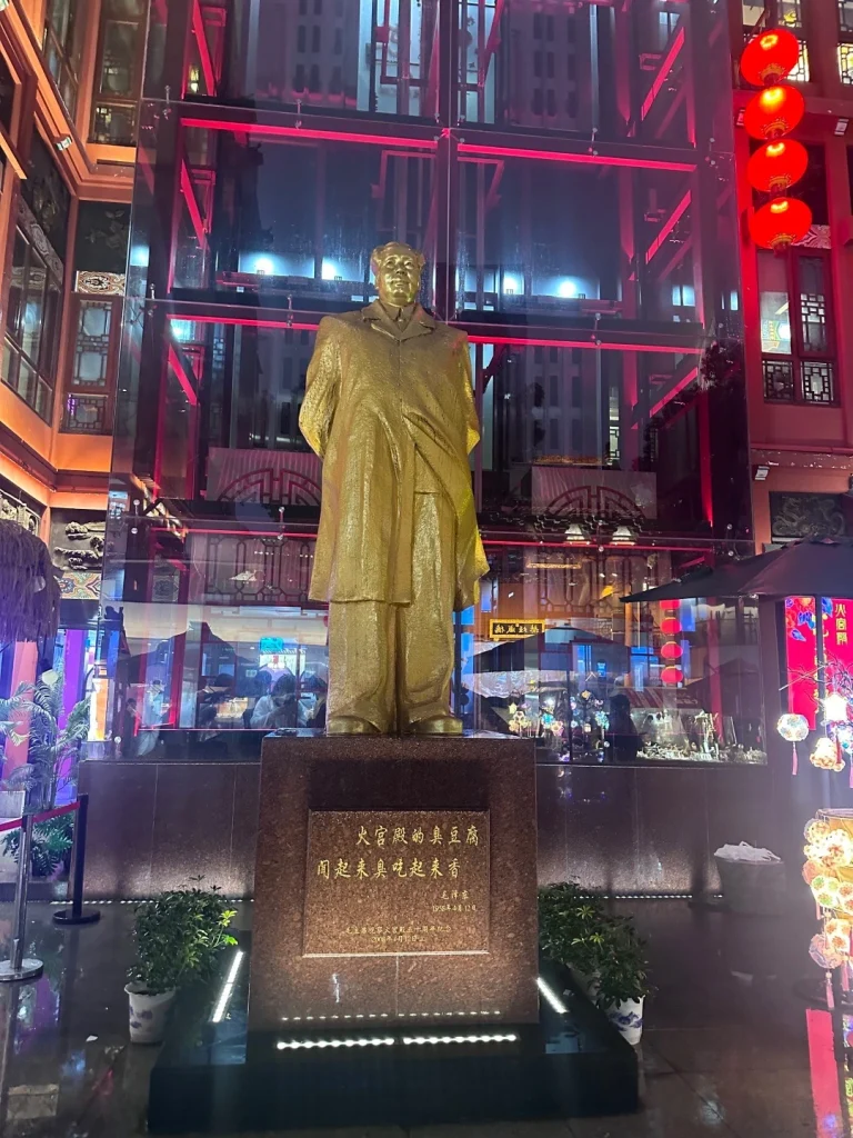 A golden statue of Mao Zedong at Fire Palace Changsha illuminated by vibrant lights and festive decorations