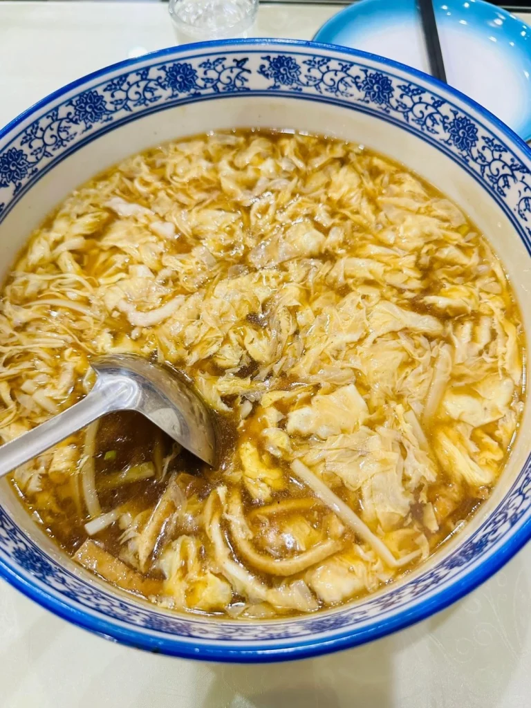 A warm bowl of flavorful soup with shredded vegetables and broth served at Jufengde restaurant