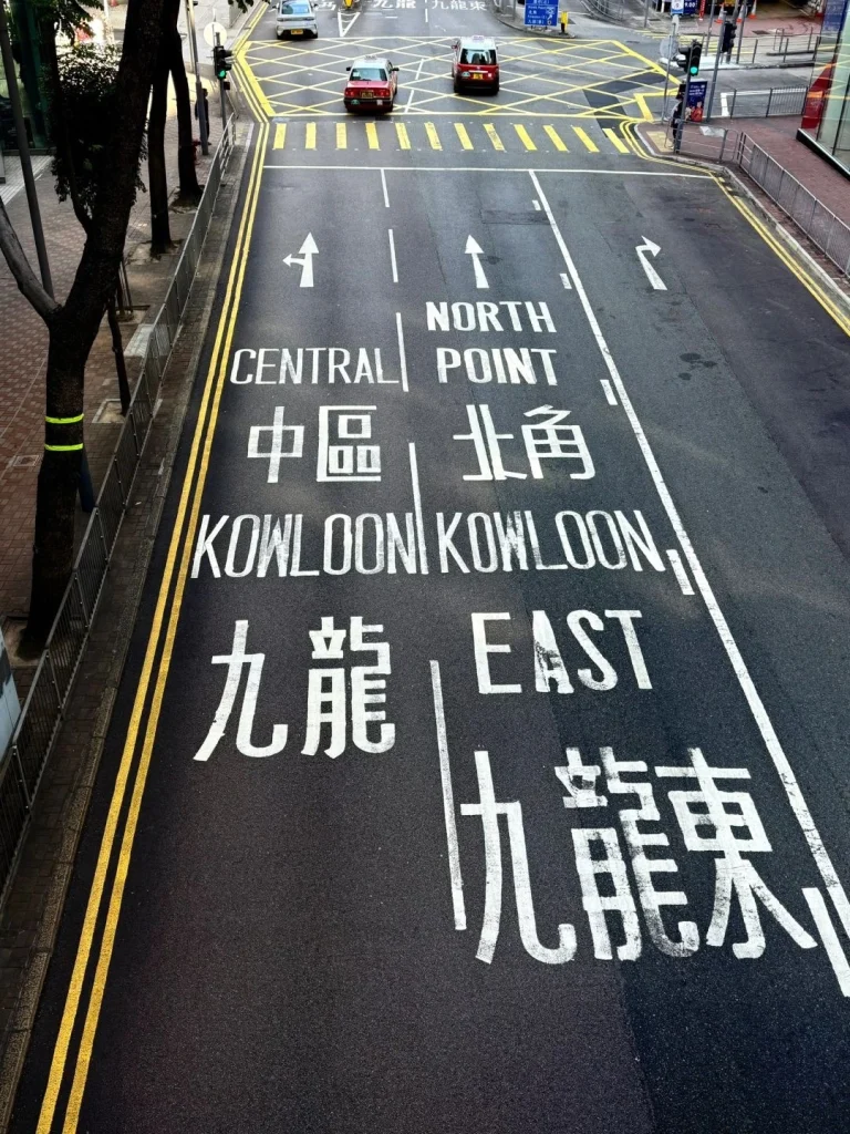 A wide shot of a busy street in Hong Kong with road signs in both English and Chinese showing traffic flow