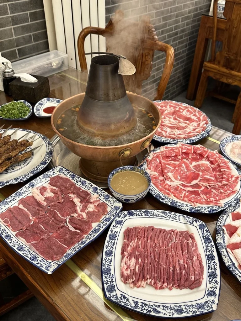 Beijing Copper Pot Hot Pot A steaming copper pot filled with broth surrounded by a variety of fresh meats vegetables and dipping sauces