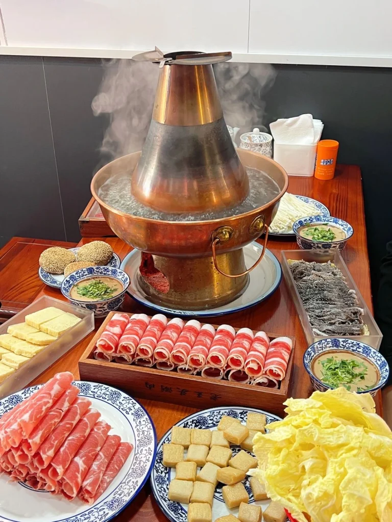 Beijing Copper Pot Hot Pot Sliced lamb and beef with fresh vegetables and dipping sauces around a simmering copper pot in a Beijing restaurant