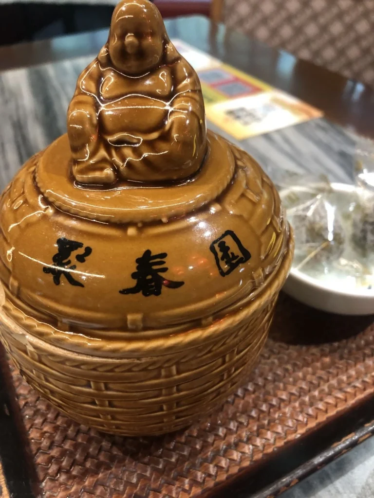 Buddhist statue at Juchun Garden A ceramic statue of a smiling Buddha placed atop a jar at Juchun Garden with a pink flower tree decorating the scene inside the restaurant