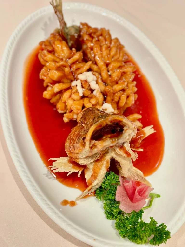 Close up of a fish dish at Deyue Lou A beautifully plated fried fish with a vibrant red sauce and garnishes