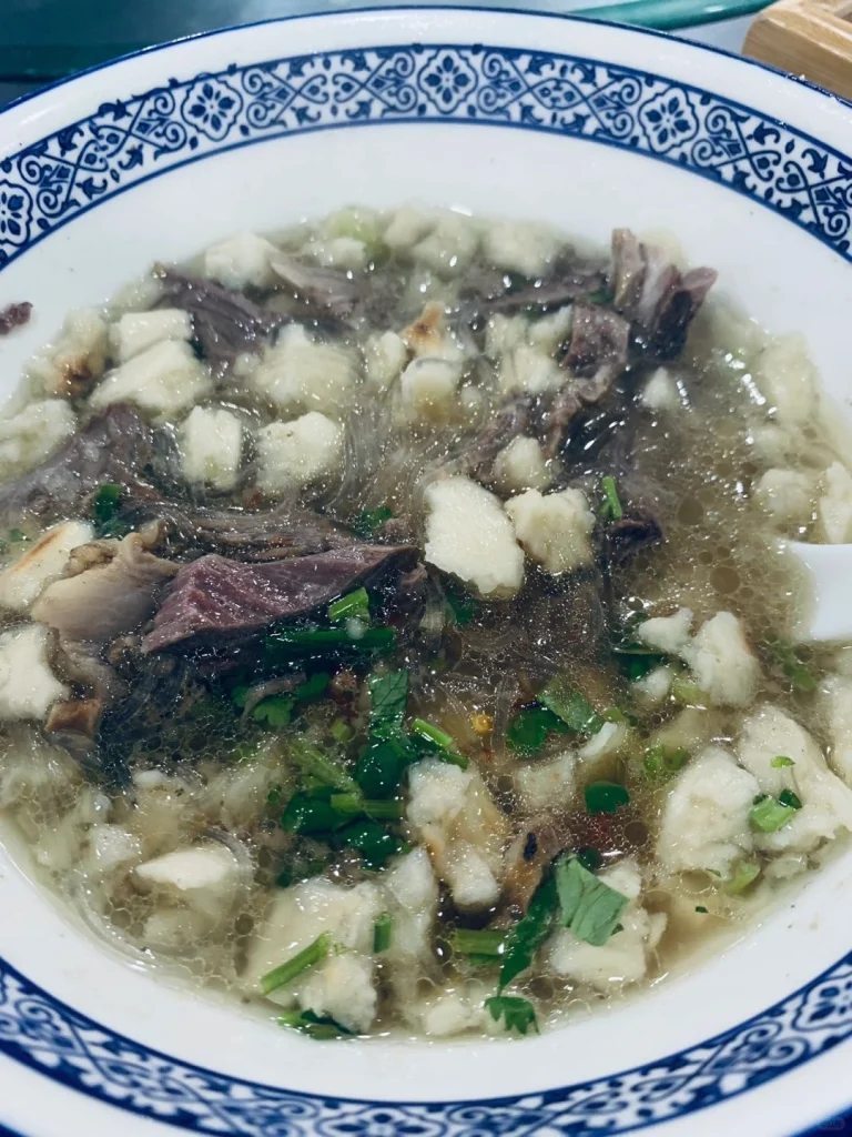 Close up shot of lamb soup at Laosunjia Restaurant featuring fresh herbs and tender meat