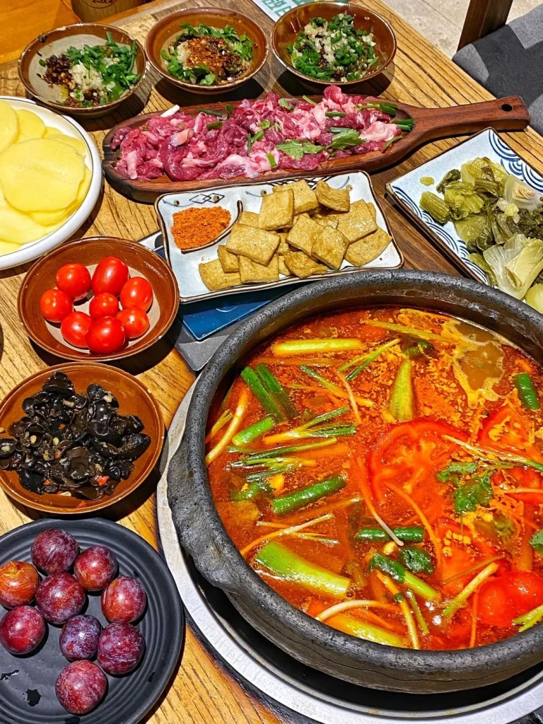 Guizhou Sour Soup Hot Pot Setup Sliced meats greens and a rich colored soup