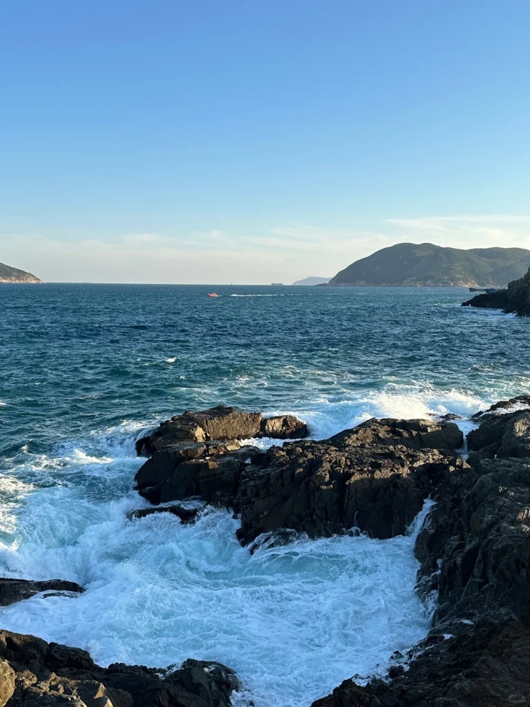Hong Kong coastline with waves and rocks Stunning coastal view of Hong Kongs rocky shore with waves crashing and a distant view of rolling hills