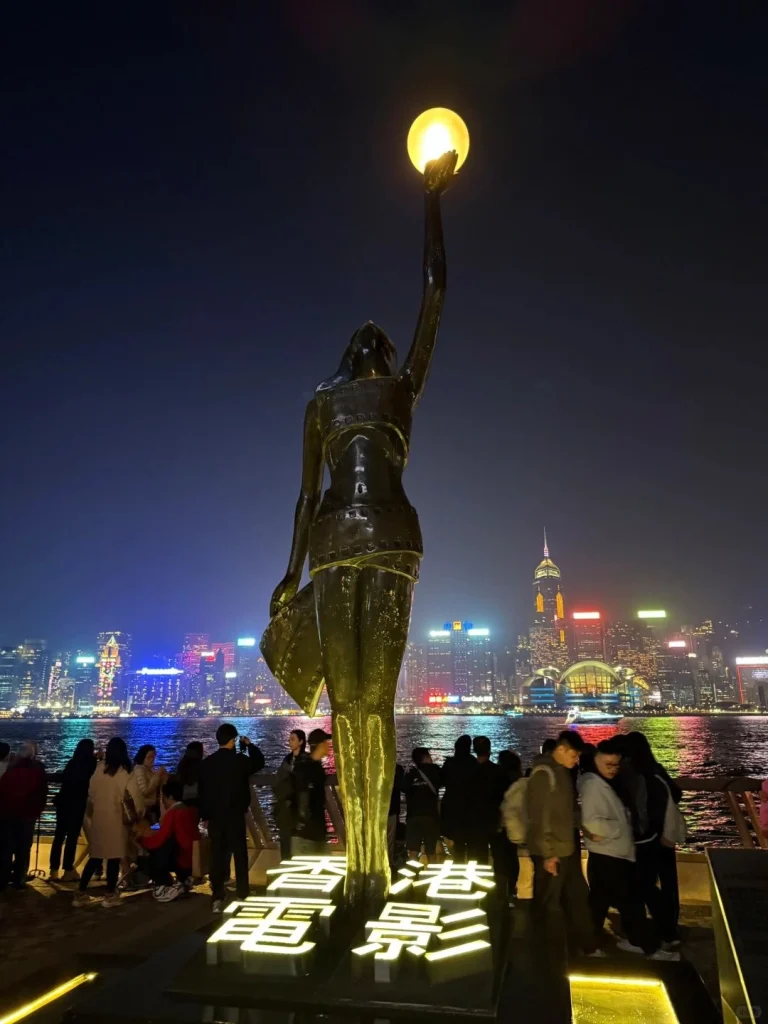 Hong Kong light sculpture at night A striking statue holding a glowing orb with Hong Kongs skyline illuminated in the background at night
