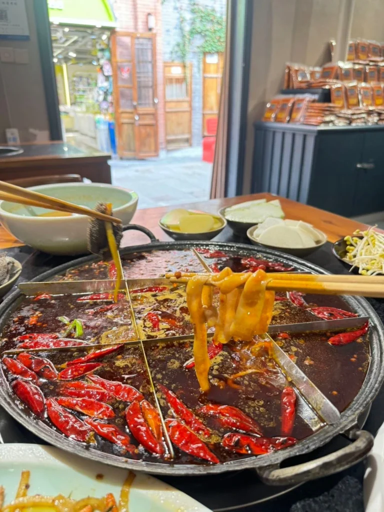 Hotpot broth with chili peppers meat and vegetables being dipped into the boiling mixture