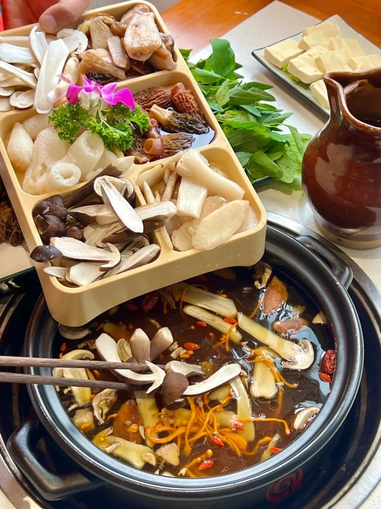 Yunnan mushroom hotpot with fresh mushrooms vegetables and herbs served in a rich broth