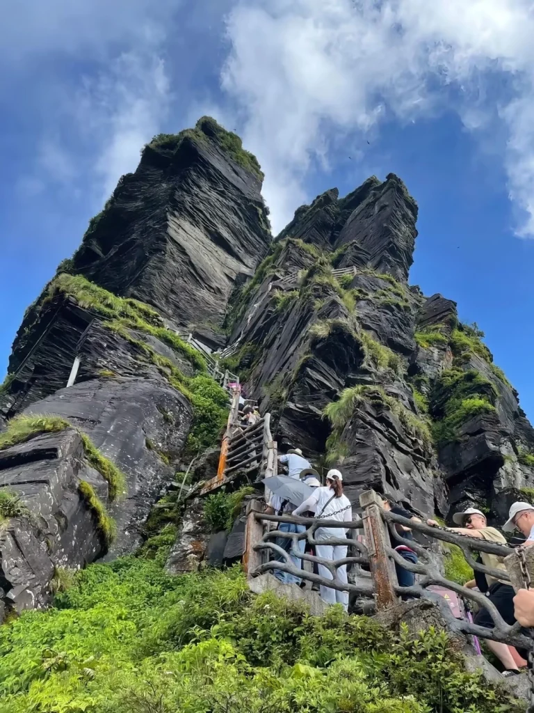 Visitors climbing steep wooden stairs up rugged cliffs of Fanjing Mountain summit