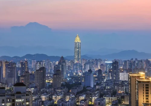 Die Skyline von Wenzhou in der Abenddämmerung: Beleuchtete Gebäude und ein hoch aufragender Wolkenkratzer vor der Kulisse von Bergen und farbenprächtigem Himmel – China-Reiseführer, Stadtführungen & Kulturtipps – The China Journey Die Skyline von Wenzhou in der Abenddämmerung: Beleuchtete Gebäude und ein hoch aufragender Wolkenkratzer vor der Kulisse von Bergen und farbenprächtigem Himmel – China-Reiseführer, Stadtführungen & Kulturtipps – The China Journey