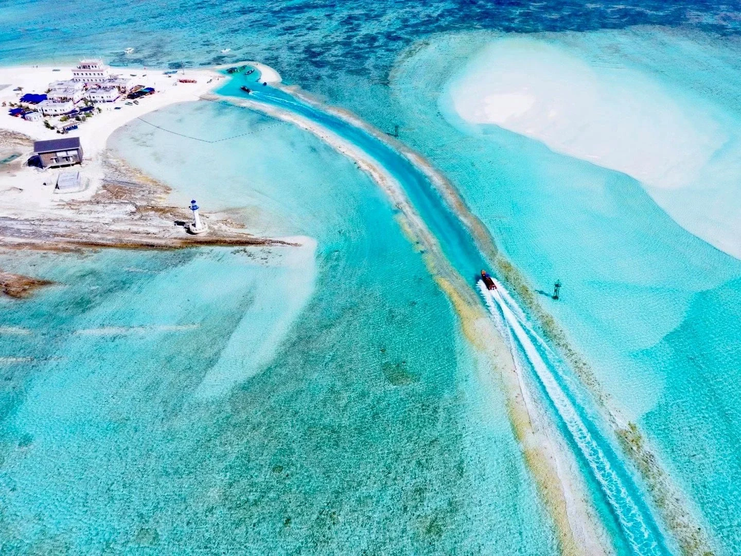 Vista aérea de las islas Xisha. Aguas turquesas cristalinas, islotes arenosos y un barco veloz cerca de un faro en el Mar de China Meridional.