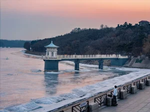 Changchun, Jilin: Friedliche Winterlandschaft mit einer schneebedeckten Brücke und einem zugefrorenen Fluss bei Sonnenuntergang in Changchun, die die friedvolle Schönheit der Stadt unterstreicht. – China-Reiseführer, Stadtführungen & Kulturtipps – The China Journey Changchun, Jilin: Friedliche Winterlandschaft mit einer schneebedeckten Brücke und einem zugefrorenen Fluss bei Sonnenuntergang in Changchun, die die friedvolle Schönheit der Stadt unterstreicht. – China-Reiseführer, Stadtführungen & Kulturtipps – The China Journey