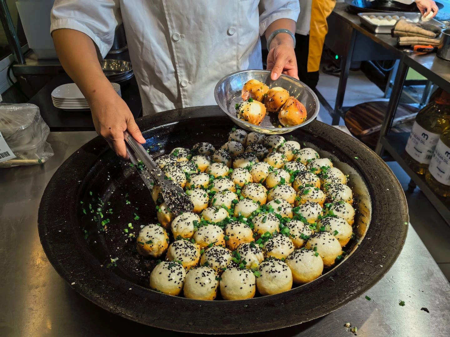 Chef bereidt Shengjian Bao in een grote pan – Een straatverkoper in Shanghai bakt tientallen Shengjian Bao in een brede ijzeren koekenpan, gegarneerd met sesamzaad en lente-uitjes. - Wat is het populairste gerecht in Shanghai, China? 2026 - De reis door China Chef bereidt Shengjian Bao in een grote pan – Een straatverkoper in Shanghai bakt tientallen Shengjian Bao in een brede ijzeren koekenpan, gegarneerd met sesamzaad en lente-uitjes. - Wat is het populairste gerecht in Shanghai, China? 2026 - De reis door China