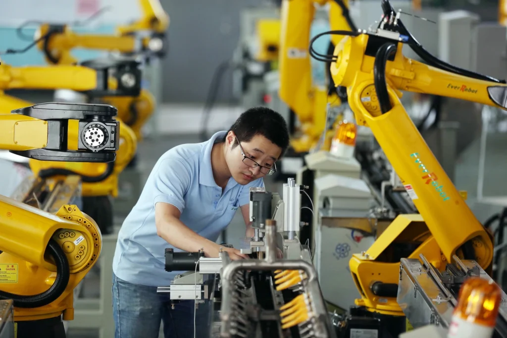 Industrial robot working in a factory A worker adjusts an industrial robot in a high tech manufacturing facility with yellow robotic arms at work.