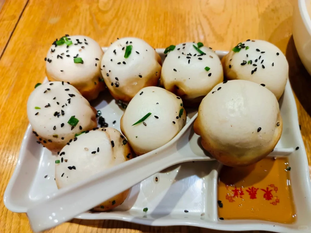 Shengjian Bao Platter on Wooden Table – Golden, juicy Shengjian Bao neatly arranged in a dish with scallions and sesame seeds, ready to enjoy.