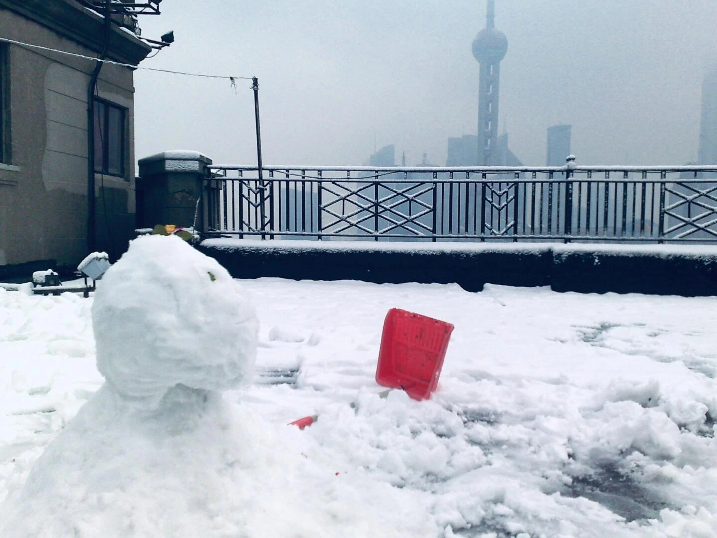 Snowman on Rooftop with Shanghai Skyline – Small snowman and red bucket on a snowy rooftop with Oriental Pearl Tower in the misty background. - Does It Snow in Shanghai? Winter Climate & Snowfall Explained 2026 - The China Journey Snowman on Rooftop with Shanghai Skyline – Small snowman and red bucket on a snowy rooftop with Oriental Pearl Tower in the misty background. - Does It Snow in Shanghai? Winter Climate & Snowfall Explained 2026 - The China Journey