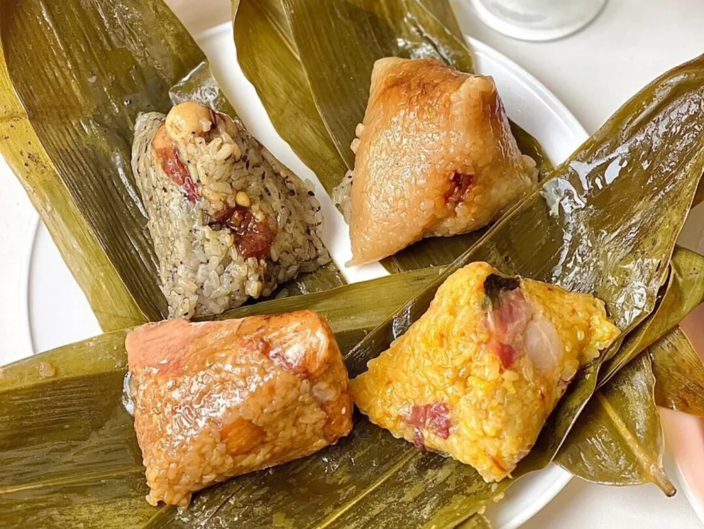 Assorted Zongzi on leaf wrappers – colorful sweet and savory sticky rice dumplings on a white plate, popular during the Dragon Boat Festival. - Chinese Holidays and Festivals in 2026: Dates, Traditions & Travel Guide - The China Journey Assorted Zongzi on leaf wrappers – colorful sweet and savory sticky rice dumplings on a white plate, popular during the Dragon Boat Festival. - Chinese Holidays and Festivals in 2026: Dates, Traditions & Travel Guide - The China Journey