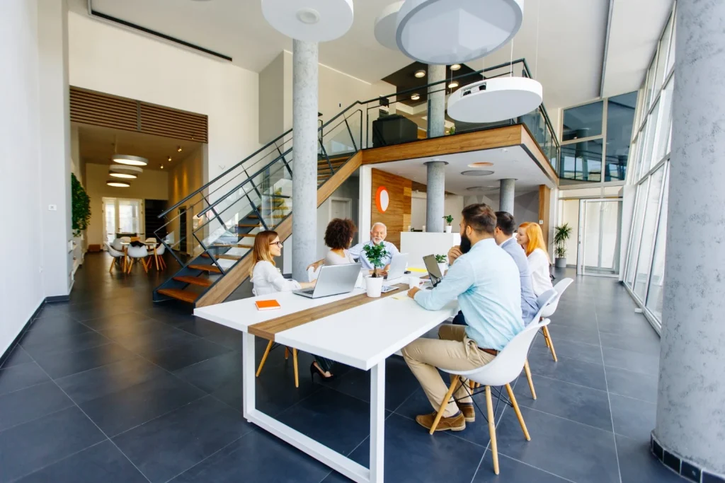 Team meeting near staircase in open office – Open concept office with good lighting, collaboration zone, and energetic Qi flow around central stairs.