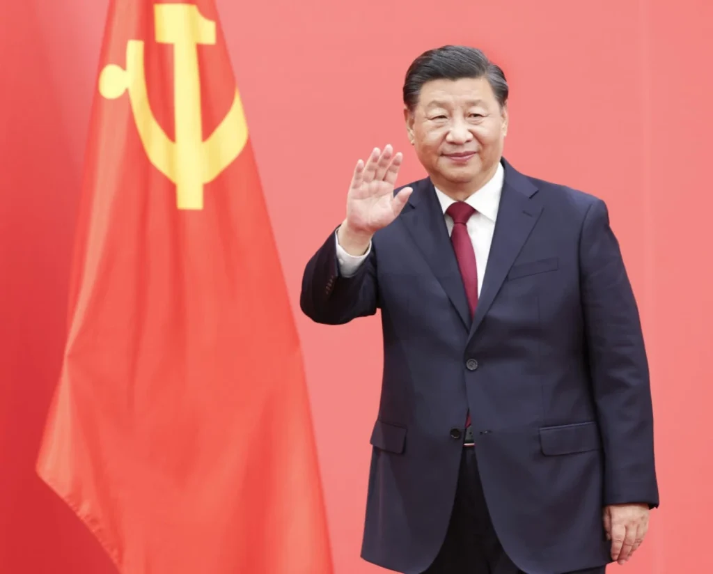 Xi Jinping and Communist Party Flag – Xi Jinping waves in front of Chinese Communist Party emblem on
