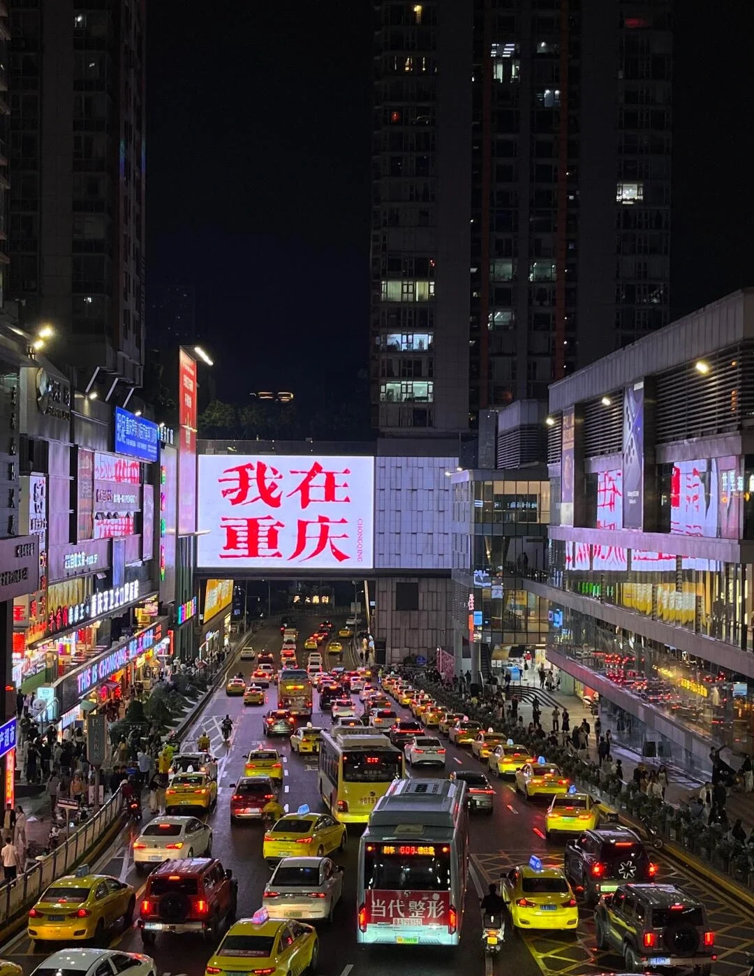 Tráfico nocturno en Guanyinqiao con taxis amarillos y grandes pantallas LED que muestran "Estoy en Chongqing - 3 días en Chongqing: el mejor itinerario para quienes visitan la ciudad por primera vez en 2026 - The China Journey". Tráfico nocturno en Guanyinqiao con taxis amarillos y grandes pantallas LED que muestran "Estoy en Chongqing - 3 días en Chongqing: el mejor itinerario para quienes visitan la ciudad por primera vez en 2026 - The China Journey".
