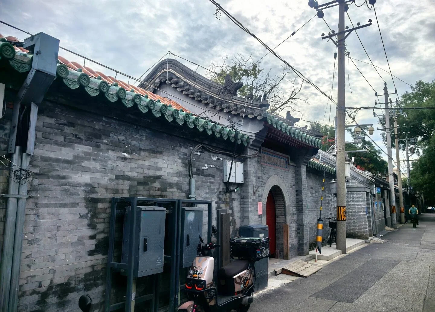 De binnenplaatsmuur van Zhuanta Hutong, een lange gevel van grijze bakstenen met groene geglazuurde tegels en een rode boogdeur, met een geparkeerde scooter ervoor - 5 dagen in Beijing: Beste reisroute voor een eerste bezoek in 2026 - The China Journey De binnenplaatsmuur van Zhuanta Hutong, een lange gevel van grijze bakstenen met groene geglazuurde tegels en een rode boogdeur, met een geparkeerde scooter ervoor - 5 dagen in Beijing: Beste reisroute voor een eerste bezoek in 2026 - The China Journey