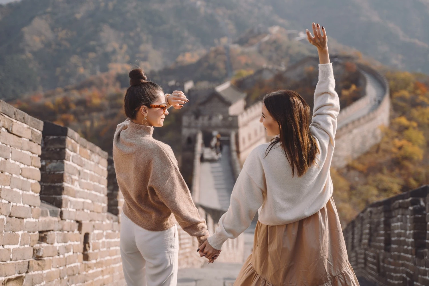Two women holding hands on the Great Wall of China, autumn mountains in background – joyful friendship travel experience. - China Packing List 2026: What to Pack for Your Trip - The China Journey Two women holding hands on the Great Wall of China, autumn mountains in background – joyful friendship travel experience. - China Packing List 2026: What to Pack for Your Trip - The China Journey