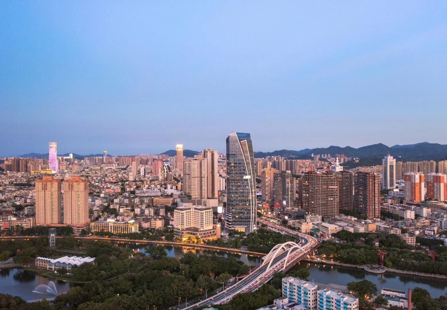Luchtfoto van de stad Zhongshan, nabij Zhuhai, met moderne hoogbouw en de schilderachtige brug over de Qijiang-rivier in de schemering